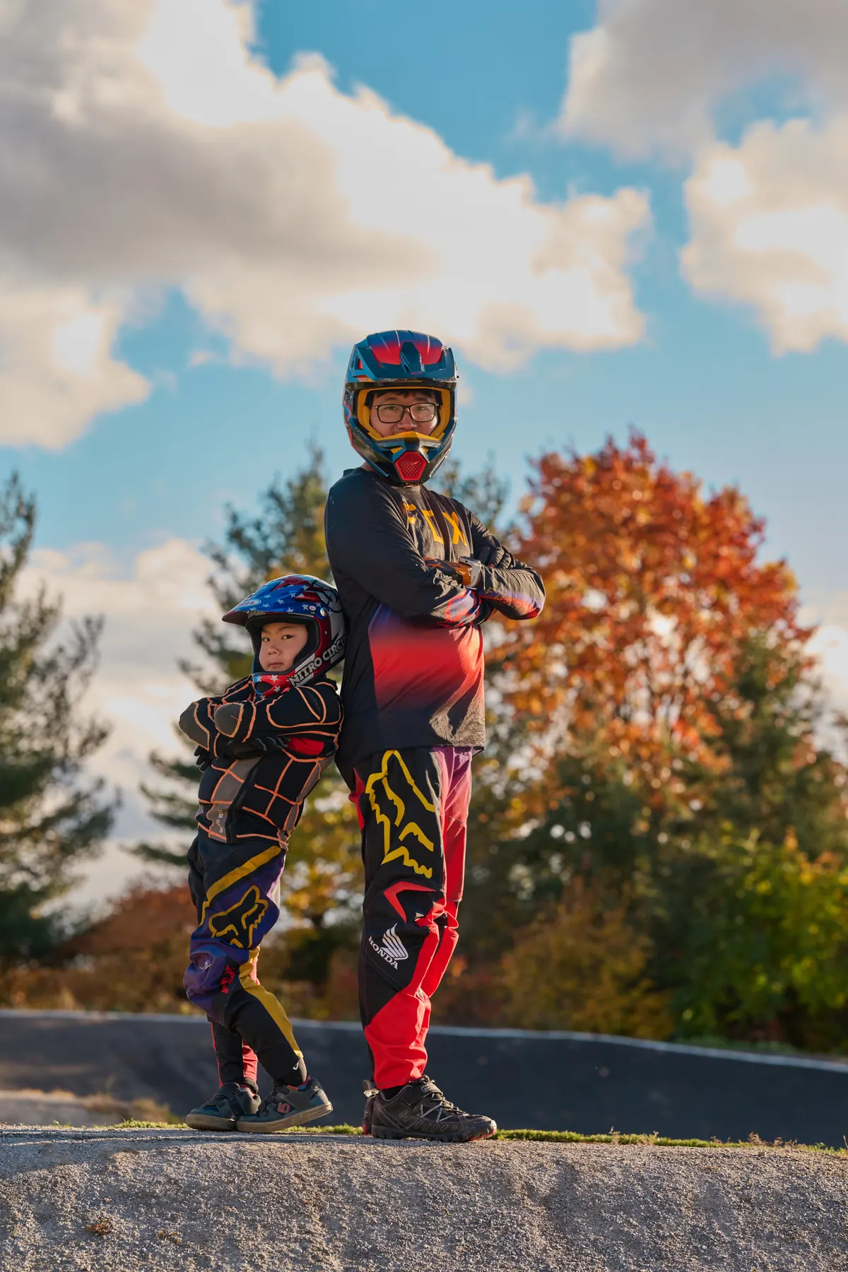 Young XKIDS BMX riders standing with bikes in race jerseys, vertical frame.