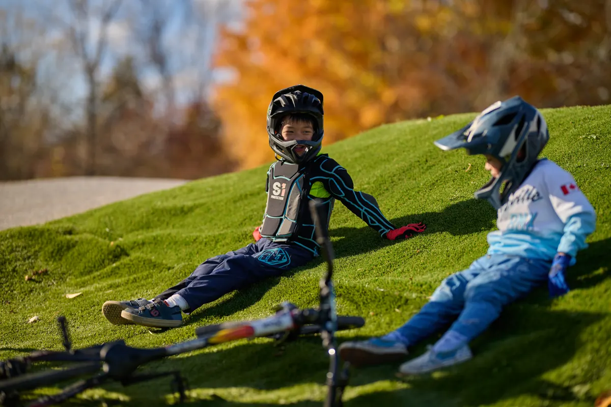 两位 XKIDS 小骑手在 BMX 赛道边休息,画面温馨。