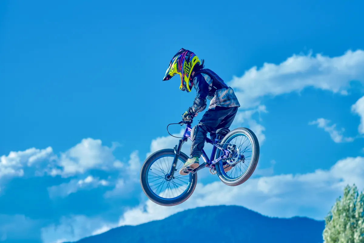 A young XKIDS mountain bike rider jumping over a dirt feature on a trail.