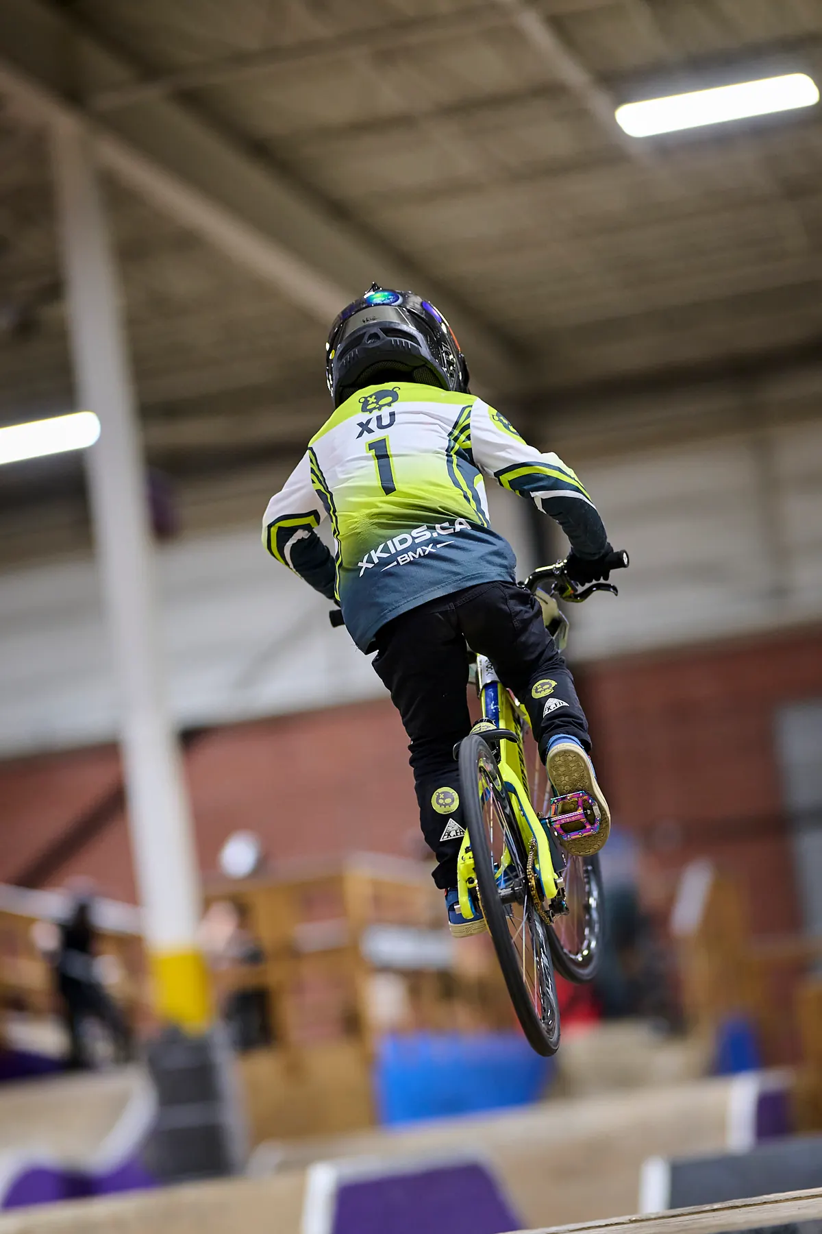 XKIDS 小骑手身穿比赛骑行服,在室内 BMX 场地腾空跃起。